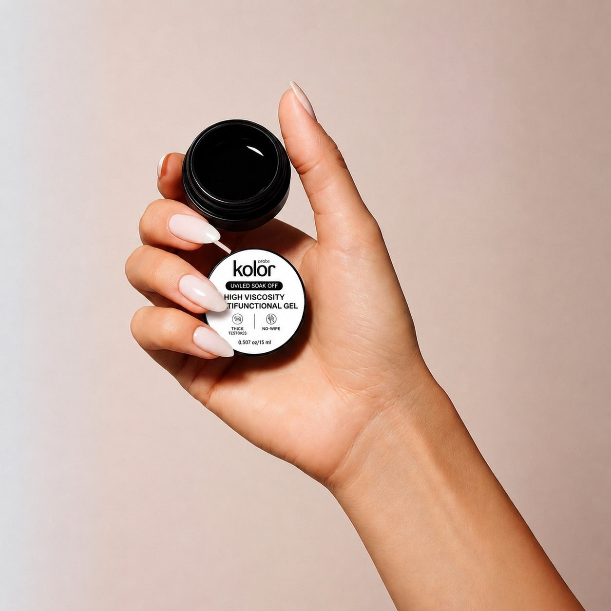 A hand with long, manicured nails holds an open black jar of Kolor High Viscosity Nail Functional Gel against a soft beige background.